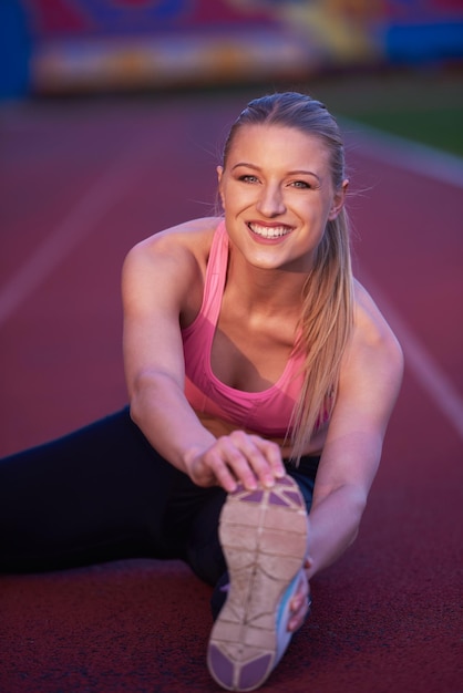 jonge runner sportieve vrouw ontspannen en strekken op atletische racebaan