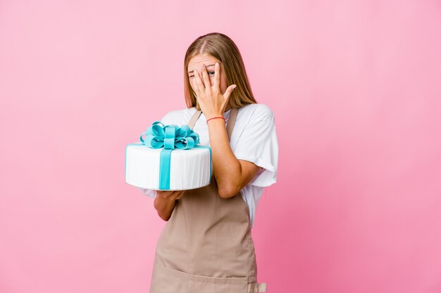 Jonge russische bakkersvrouw die een heerlijke cake vasthoudt, knippert bang en nerveus door vingers.