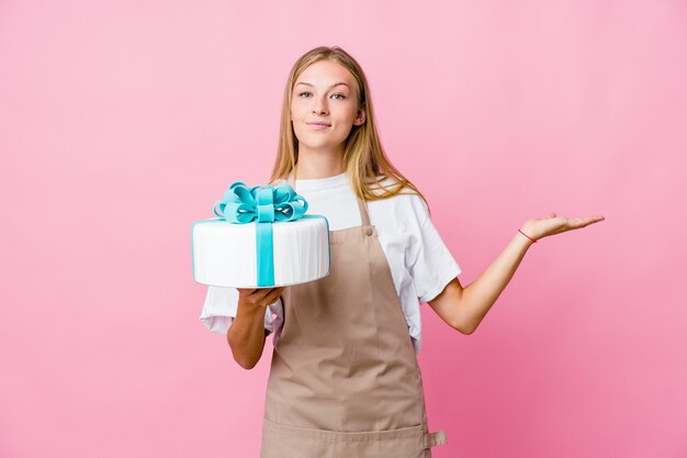 Jonge Russische bakkersvrouw met een heerlijke cake maakt schaal met armen, voelt zich gelukkig en zelfverzekerd