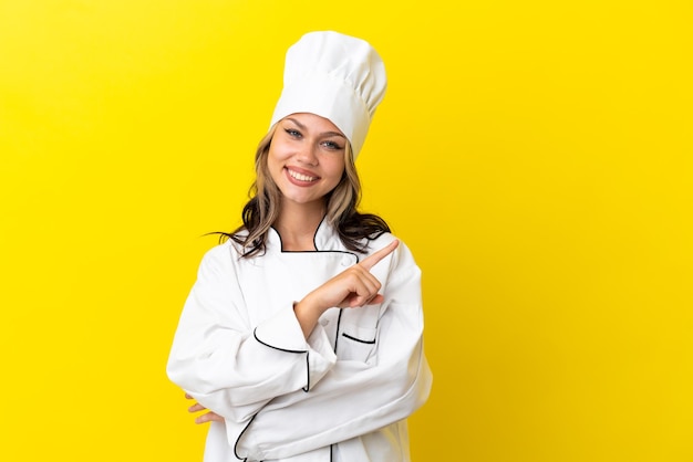 Jonge russische chef-kok geïsoleerd op een gele achtergrond die naar de zijkant wijst om een product te presenteren