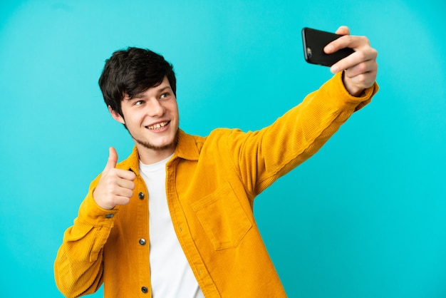 Jonge Russische man geïsoleerd op blauwe achtergrond die een selfie maakt met mobiele telefoon