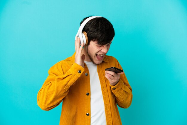 Jonge Russische man geïsoleerd op blauwe achtergrond muziek luisteren met een mobiel en zingen