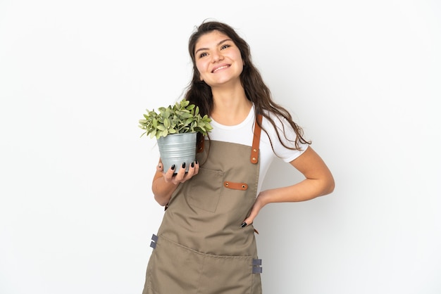 Jonge Russische tuinman meisje met een plant geïsoleerd poseren met armen op heup en glimlachen