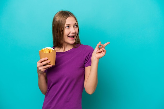 Jonge Russische vrouw die frietjes vangt die op een blauwe achtergrond zijn geïsoleerd en die de oplossing wil realiseren terwijl ze een vinger opsteekt