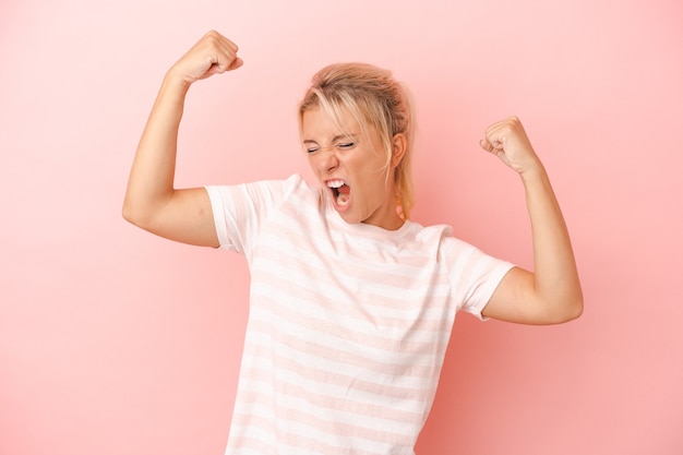 Foto jonge russische vrouw die op roze achtergrond wordt geïsoleerd die vuist opheft na een overwinning, winnaarconcept.