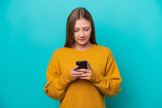 Jonge Russische vrouw geïsoleerd op blauwe achtergrond met behulp van mobiele telefoon