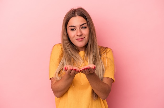 Jonge Russische vrouw geïsoleerd op roze achtergrond met iets met beide handen, productpresentatie.