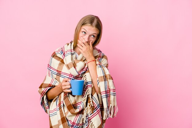 Jonge russische vrouw gewikkeld in een deken koffie drinken nadenkend op zoek naar een kopie ruimte die mond bedekt met hand.