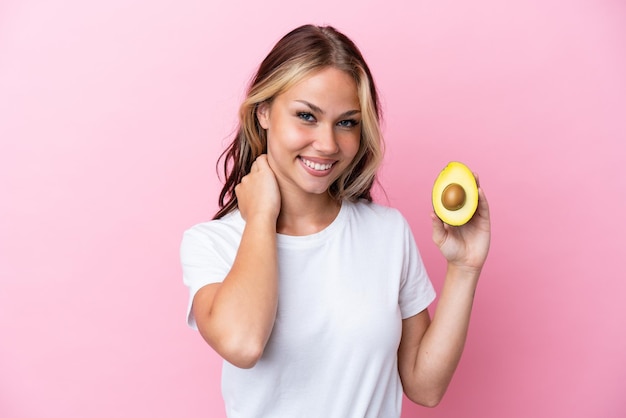 Jonge Russische vrouw met avocado geïsoleerd op roze achtergrond lachen