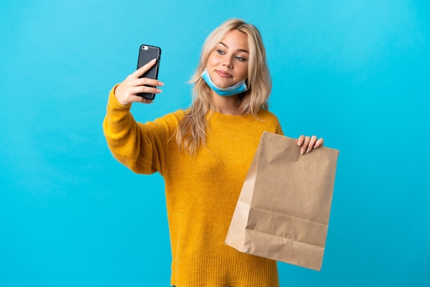 Jonge Russische vrouw met een boodschappentas geïsoleerd op blauw een selfie maken