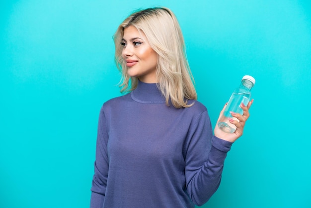 Jonge Russische vrouw met een fles water geïsoleerd op een blauwe achtergrond op zoek naar kant