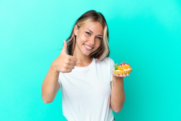 Jonge Russische vrouw met een fruitzoet geïsoleerd op een blauwe achtergrond met duimen omhoog omdat er iets goeds is gebeurd