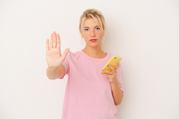 Jonge Russische vrouw met mobiele telefoon geïsoleerd op een witte achtergrond staande met uitgestrekte hand weergegeven: stopbord, waardoor u.