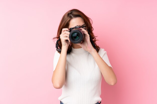 Jonge Russische vrouw over geïsoleerde roze achtergrond met een professionele camera