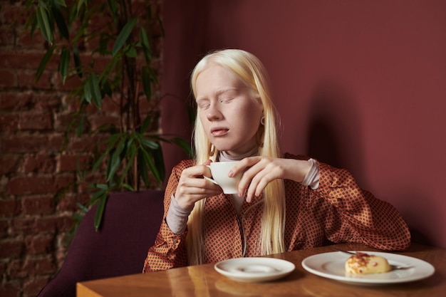 Jonge rustige albinovrouw die met lang wit haar kop van koffie houdt