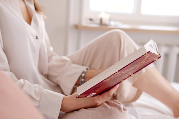 Foto jonge, rustige, gelukkige vrouw in lichte kleren. ze ligt in bed, leest een boek, studeert, ontspant zich, brengt tijd door.