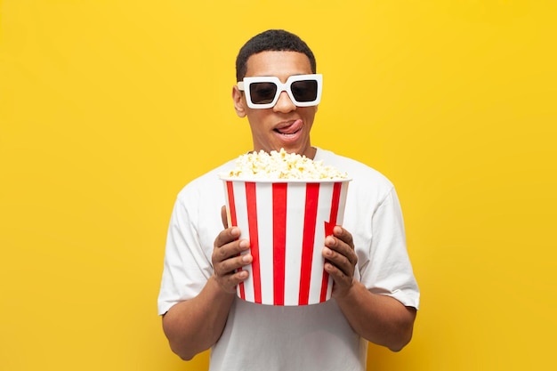 Jonge schattige Afro-Amerikaan eet popcorn en kijkt naar film op gele geïsoleerde achtergrond