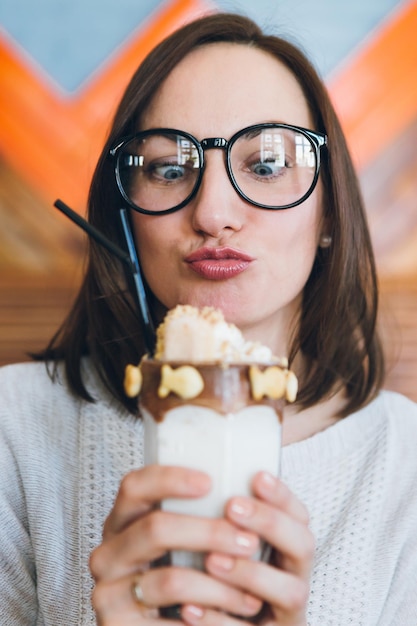 Jonge schattige brunette vrouw drinkt milkshake prachtig versierd met room en koekjes in het café. tonen.