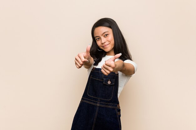 Jonge schattige chinese tiener Jonge blonde vrouw draagt een jas tegen een roze achtergrond met thumbs ups, cheers over iets, steun en respect concept.