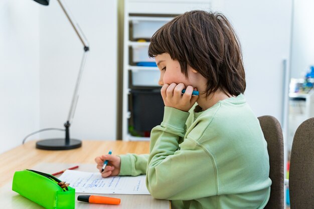 Jonge school jongen zijn huiswerk aan de tafel thuis zitten. geconcentreerd kind dat over een taak nadenkt. thuisonderwijs.