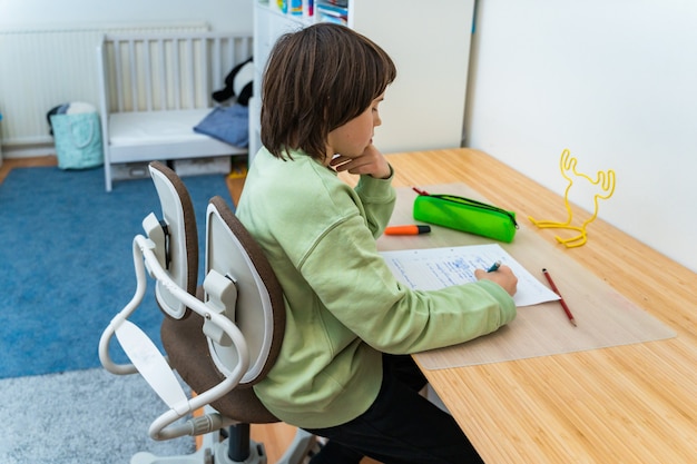 Jonge school jongen zijn huiswerk aan de tafel thuis zitten. geconcentreerd kind dat over een taak nadenkt. Thuisonderwijs.