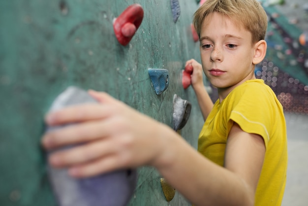 Jonge schooljongen in geel t-shirt bedrijf door kleine rotsen op klimmuur