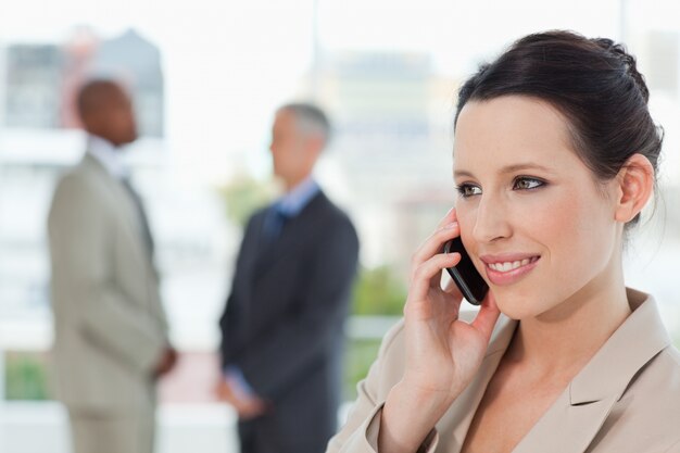 Jonge secretaresse die op de telefoon spreekt terwijl het glimlachen en het kijken naar de kant