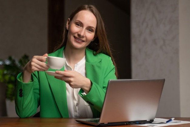 Jonge secretaresse geniet van kopje koffie werken op computer in kantoor tevreden brunette vrouw in