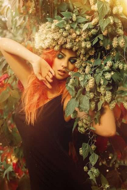 Jonge sensuele roodharige dame met hop op het hoofd en gesloten ogen in bos poseren buitenshuis