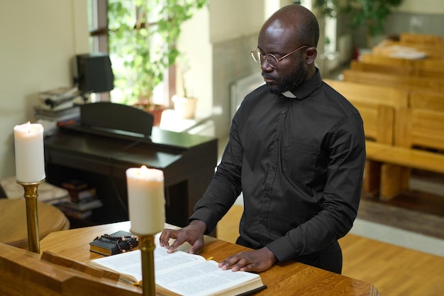 Jonge serieuze Afro-Amerikaanse predikant in zwart shirt die verzen uit de bijbel leest