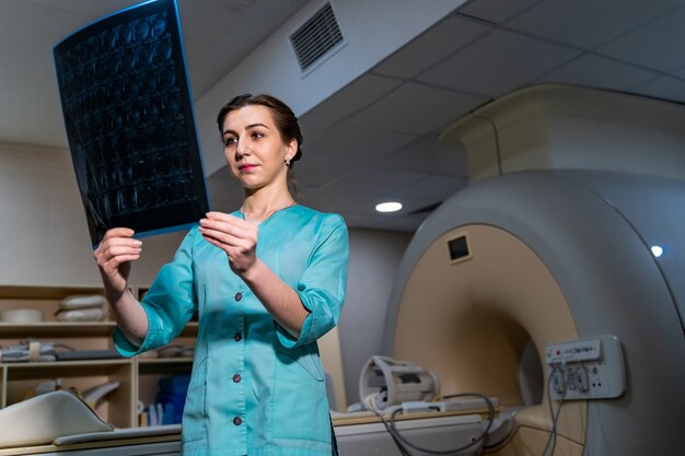 Jonge serieuze competente vrouwelijke arts die naar röntgenfoto's kijkt op het kantoor van de dokter. Computer tomografie achtergrond.