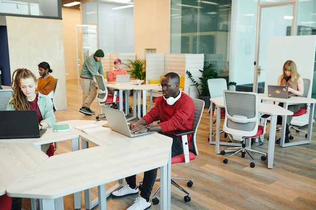 Jonge serieuze kantoormanagers of ontwerpers van verschillende etniciteiten die aan een bureau zitten en laptops gebruiken tijdens individueel werk in de open ruimte