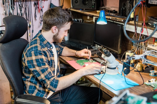 Jonge serieuze monteur of reparateur met klein stalen handgereedschap voor het repareren van een gedemonteerd touchpad of ander gadget