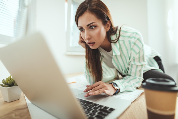 Jonge serieuze peinzende zakenvrouw werkt op de computer op kantoor. Ze maakt zich zorgen over iets dat op de laptop wordt weergegeven.