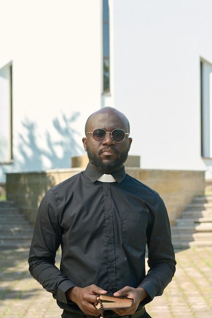 Jonge serieuze priester in zwart shirt met kerkelijke kraag met heilige bijbel