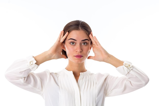 Jonge serieuze vrouw in witte blouse die haar hoofd op witte achtergrond in studio houdt