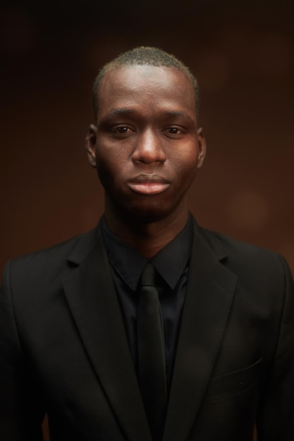Jonge serieuze zakenman van Afrikaanse etniciteit in zwarte stropdas en jas