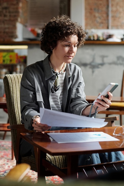 Jonge serieuze zakenvrouw sms't in mobiele telefoon terwijl ze in café werkt