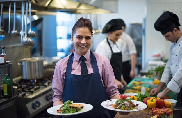 jonge serveerster die gerechten van smakelijke maaltijden presenteert in de commerciële keuken