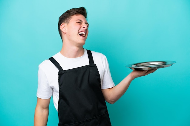 Jonge serveerster met dienblad geïsoleerd op blauwe achtergrond lachen