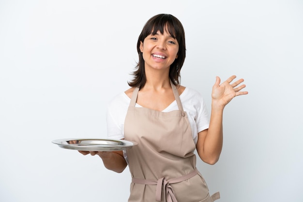 Jonge serveerster met dienblad geïsoleerd op een witte achtergrond die met de hand salueert met een gelukkige uitdrukking