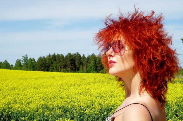 Jonge sexy blanke vrouw met rood haar en zonnebril op de gele achtergrond van het verkrachtingsveld, zomerdag