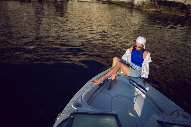 Jonge sexy vrouw in een blauwe zwembroek en korte broek zit op de boeg van een jacht in de zomer op vakantie