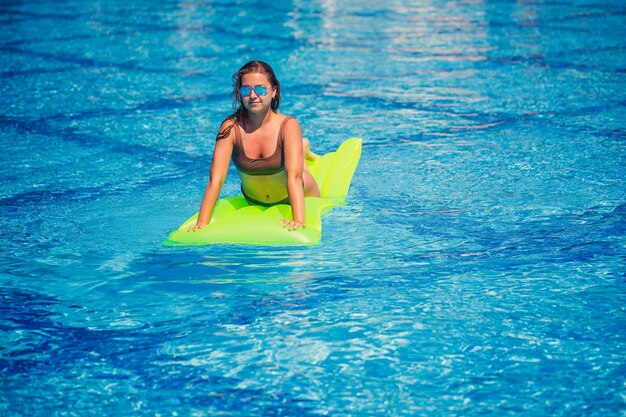 Jonge sexy vrouw in een zwembroek zwemt in het zwembad op een opblaasbare matras Meisje in zonnebril met een glimlach op gezichten in een blauw zwembad op vakantie