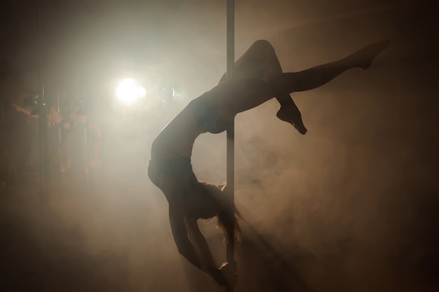 Jonge sexy vrouw oefenen pole dans op dark.