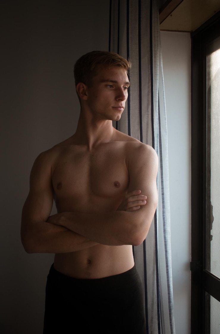 Foto jonge shirtloze man die wegkijkt terwijl hij bij het raam staat