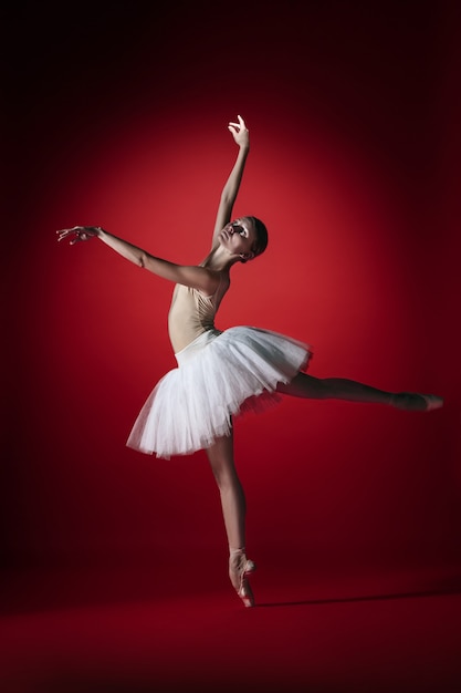 Jonge sierlijke vrouwelijke balletdanser of klassieke ballerina dansen in rode studio. Kaukasisch model op spitzen