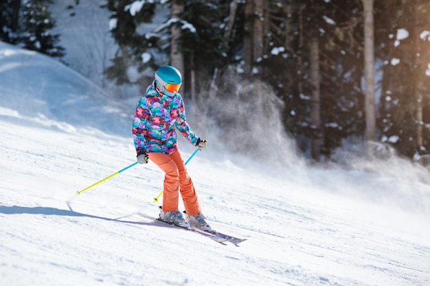 Jonge skiër in lichte kleding die op een zonnige dag in een bergresort van de helling glijdt