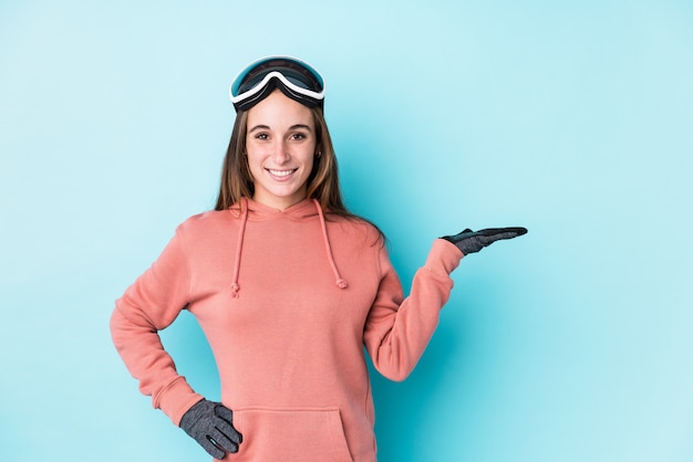 Jonge skiërvrouw die een lege ruimte op een palm toont en een andere hand op taille houdt.