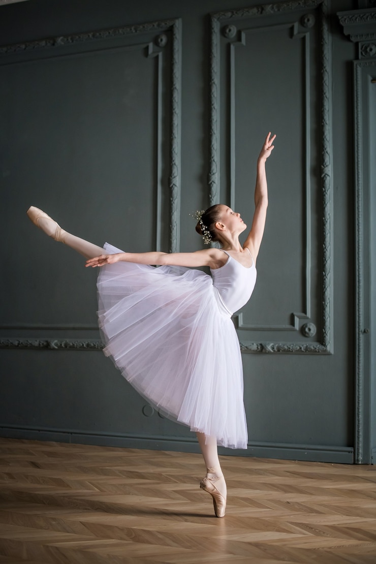 Foto jonge slanke ballerina in een witte tutu danst op pointe-schoenen in een ruime, lichte kamer met grote ramen.